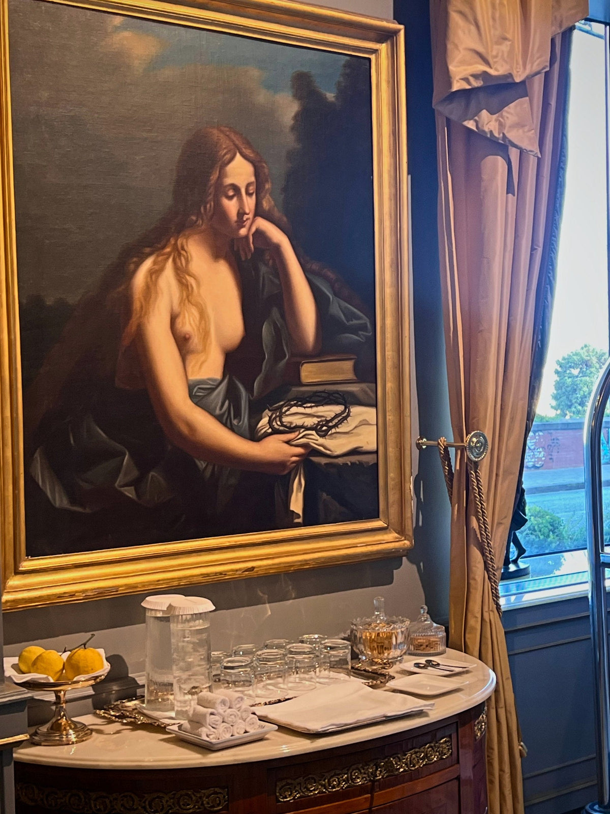 A painting of Mary Magdalene above a sideboard laid with glasses and lemons