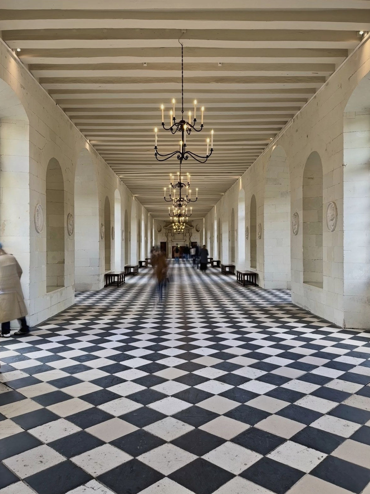 A chateau gallery with chandeliers and a checkerboard floor