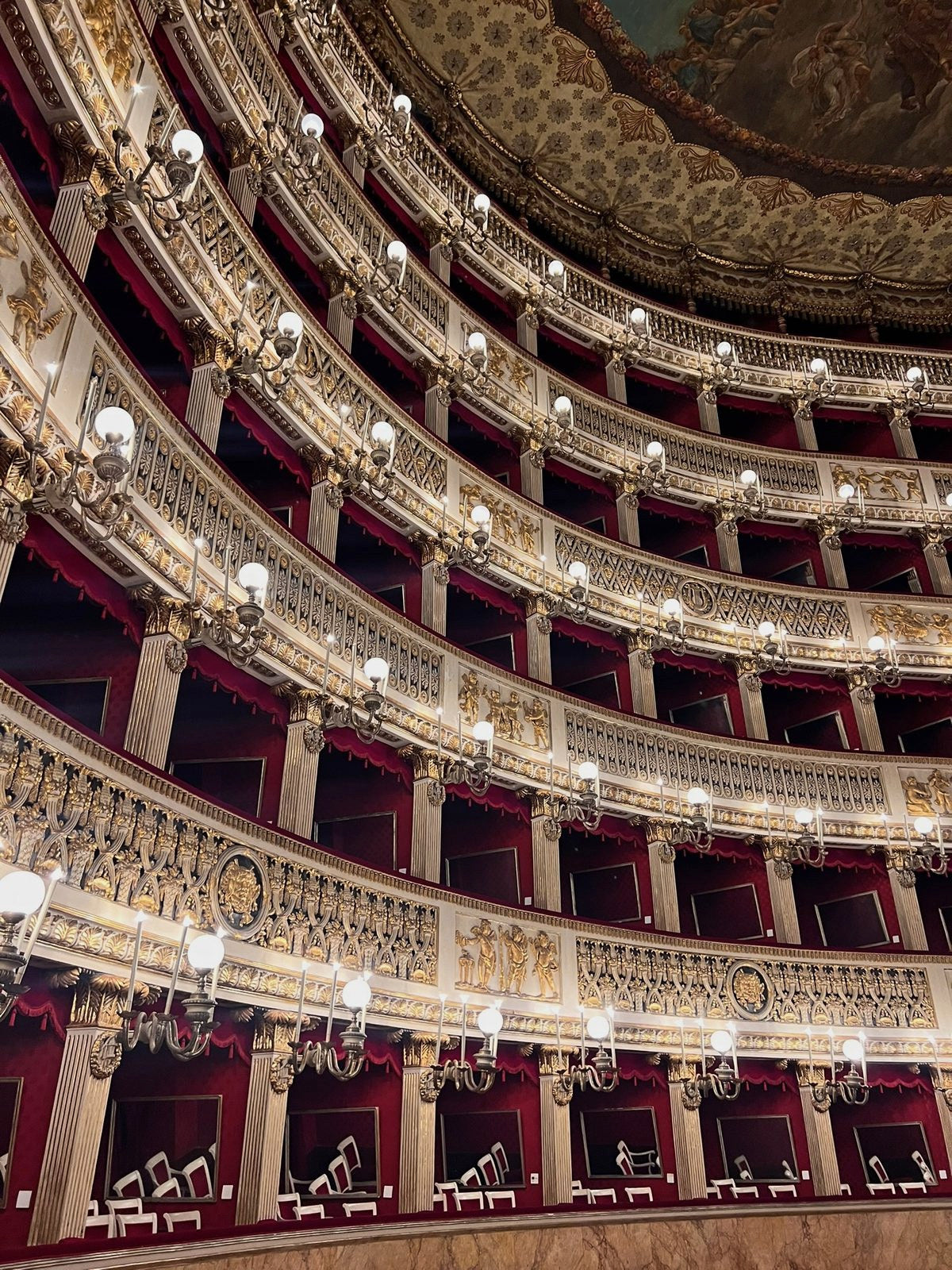 Tiers of gilded opera boxes curving up to a painted ceiling, lit by candle sconces