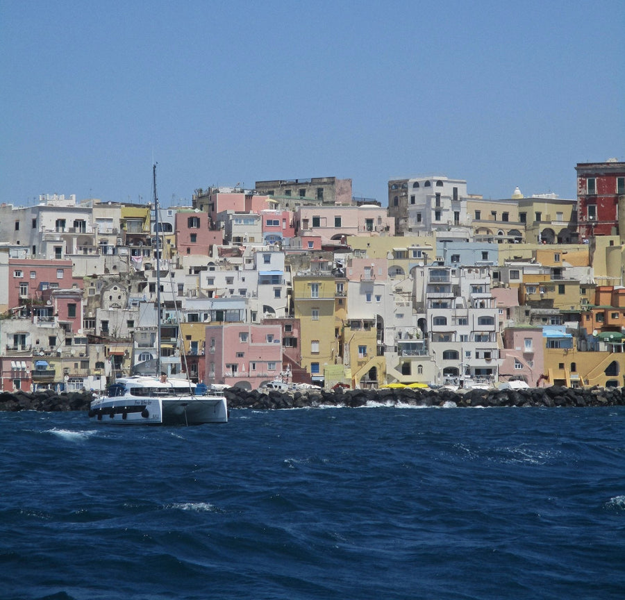 A catamaran moored off a harbour of pastel houses on an island in the Bay of Naples
