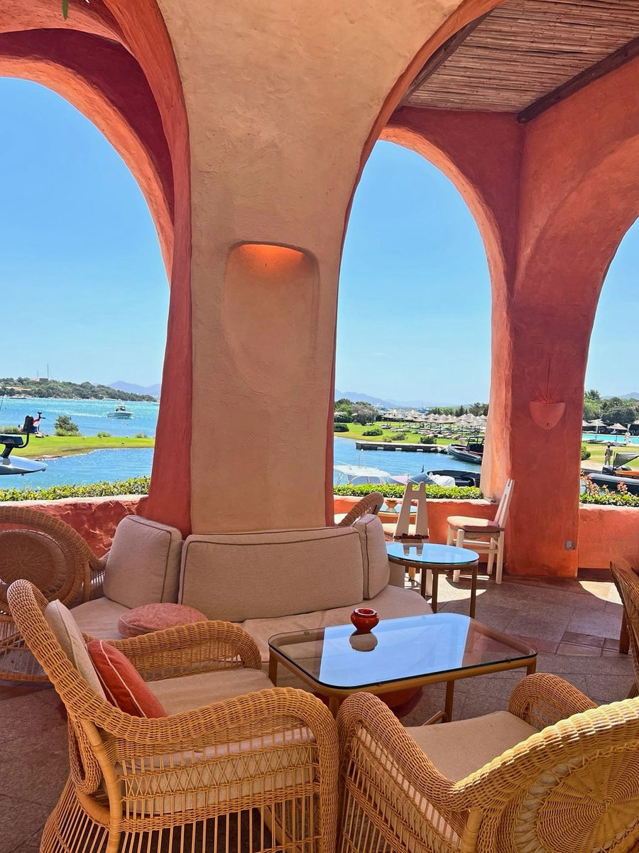 Wicker armchairs under terracotta arches looking out over a marina and lawns