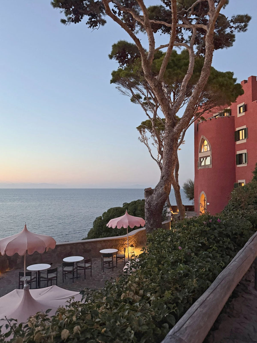 A cliffside terrace with pink parasols at sunset