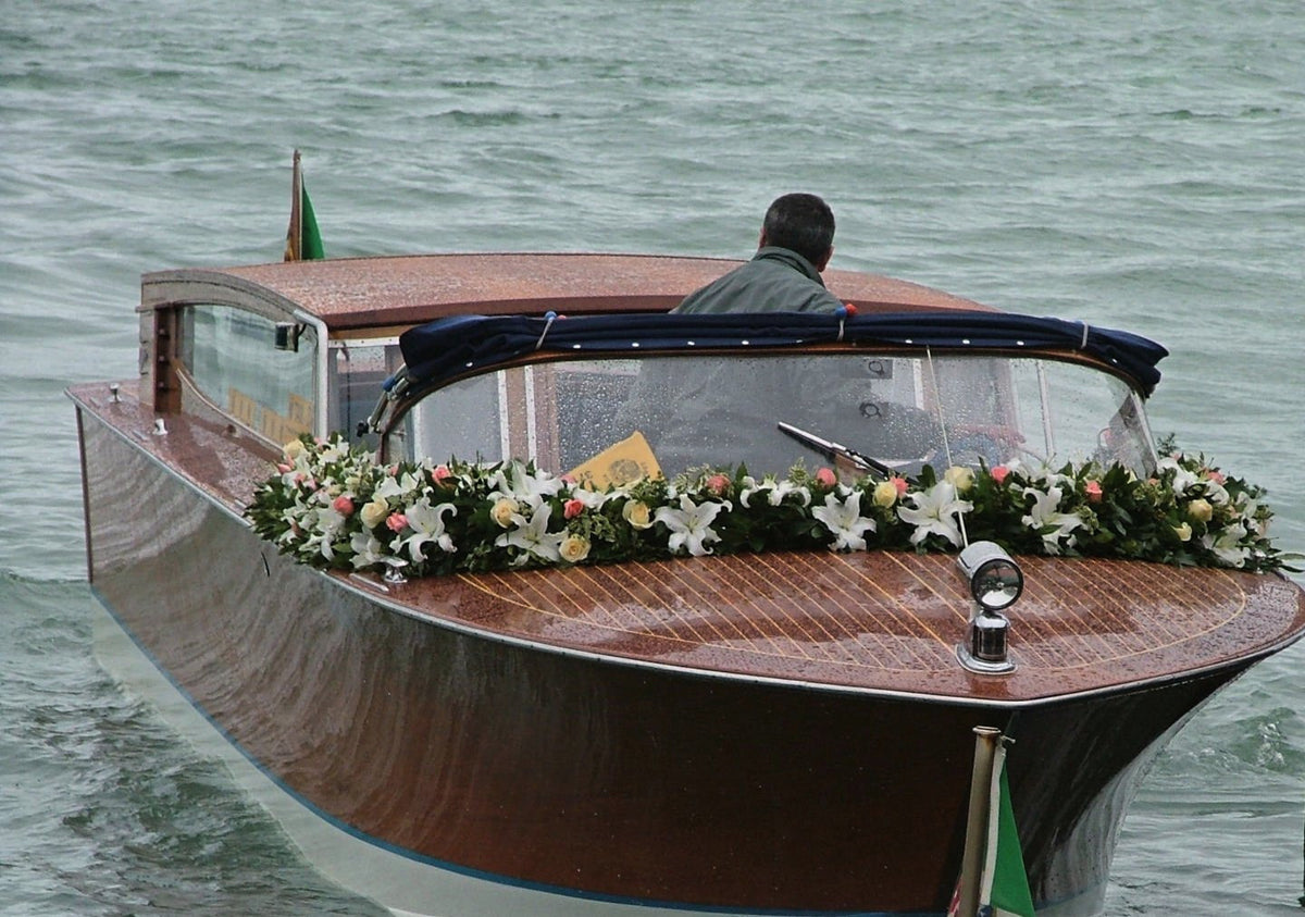A wooden water taxi dressed with a garland of roses and lilies, arriving in Venice